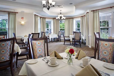 Dining room with set tables, patterned wooden chairs and tall windows.
