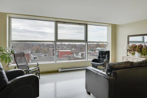 Sitting room with leather chairs, a sofa and large windows overlooking rooftops
