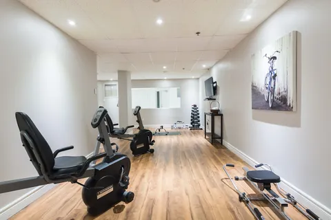 Fitness room with exercise equipment and wood flooring.