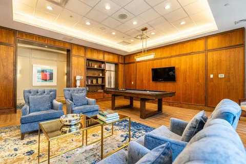 Room with a pool table, blue armchairs, a sofa and wood-panelled walls