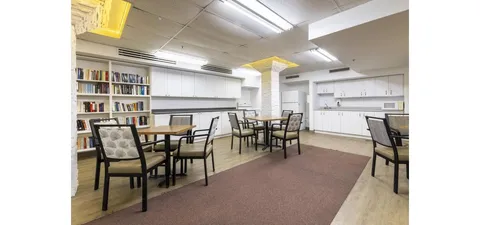 Room with bookcases, tables, patterned chairs and a white kitchenette