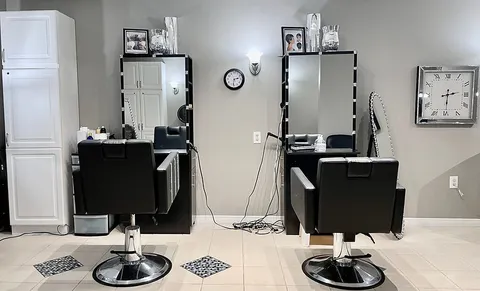 Hair salon with two styling chairs, mirrors and a sink.