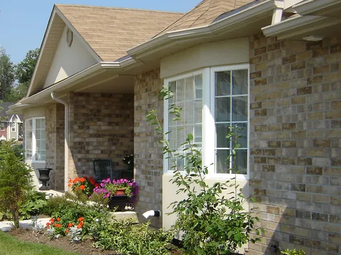 Brick bungalow exterior with a covered porch and flower beds.