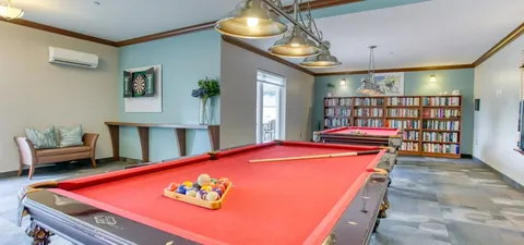 Billiards room with red tables, a dartboard and bookshelves