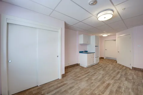 Empty room with a kitchenette, doors and wood-patterned flooring