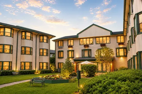 Residence exterior at dusk surrounding a lawn, benches and flower beds.