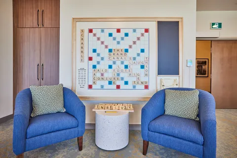 Two blue armchairs beneath a framed Scrabble board