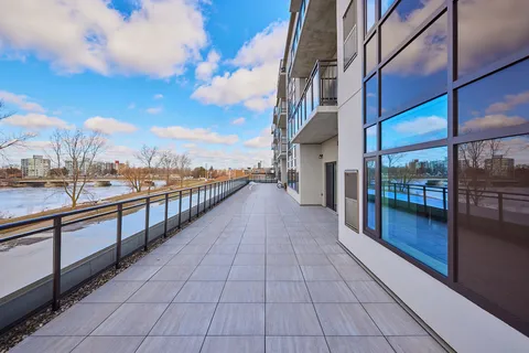 Terrace with tiled paving and a glass railing beside the building, overlooking water