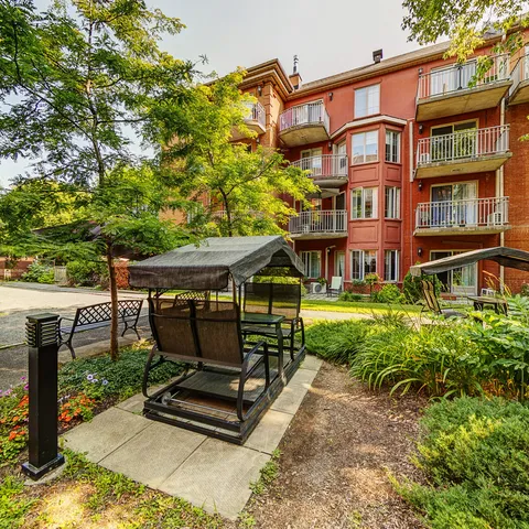 Brick residence with balconies beside garden paths, flower beds and covered bench swings