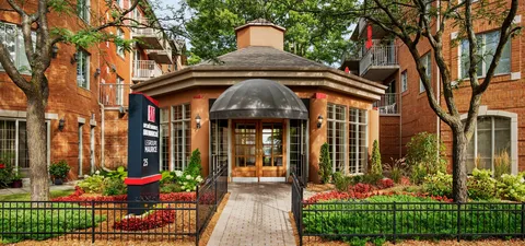 Glass entrance doors beneath a black canopy beside planted flower beds
