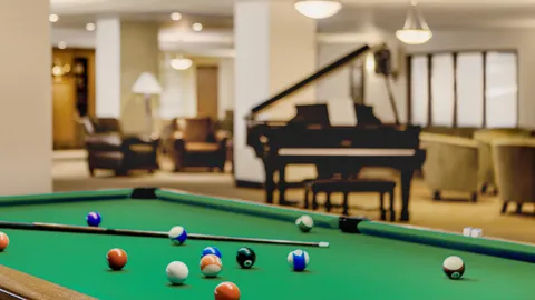 Billiard table with balls and cues beside a grand piano
