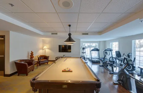 Billiard table beside armchairs and exercise machines near windows