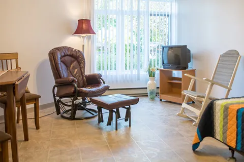 Room with a leather reclining chair, a wooden chair, a television and part of a bed