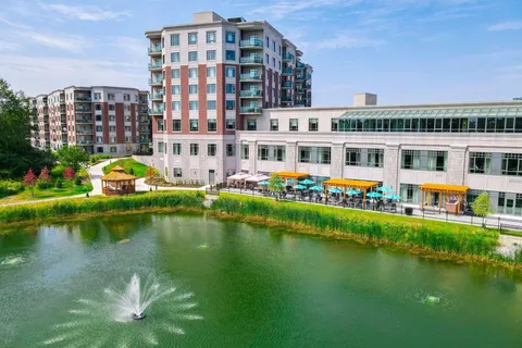 Residence buildings beside a pond with a fountain and landscaped grounds.