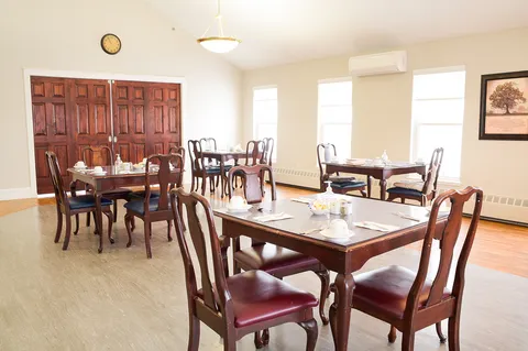 Set dining tables and wooden chairs beside wide windows and landscape pictures