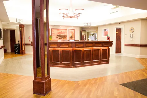 Wooden reception counter beneath a chandelier beside columns and landscape pictures