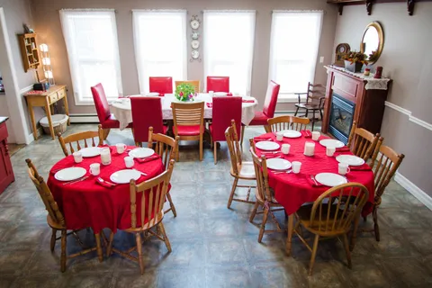 Dining room with round tables, wooden chairs and red tablecloths.