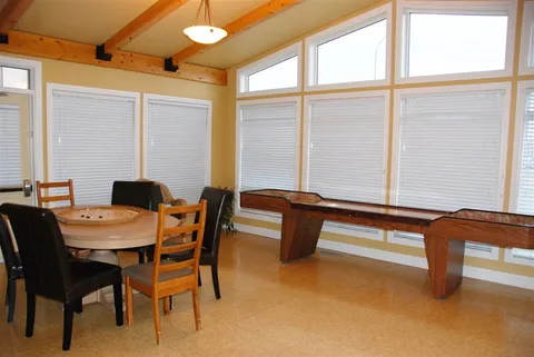 Games area with a round table and a shuffleboard table by the windows.