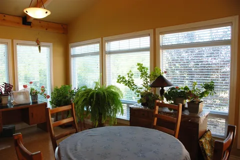 Windowed sitting area with a round table, chairs and potted plants.