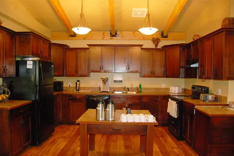 Shared kitchen with wooden cabinets and a table beneath pendant lights.