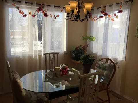 Round glass dining table and wooden chairs beside curtained windows