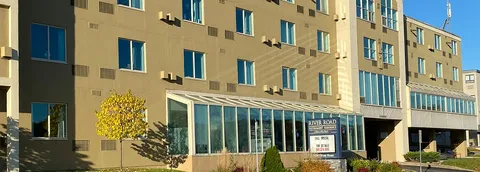 Multi-storey building with glass sunrooms, a front entrance, shrubs and a residence sign