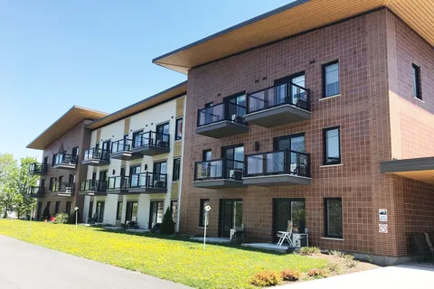 Residence exterior with brick walls, balconies, a driveway and a lawn