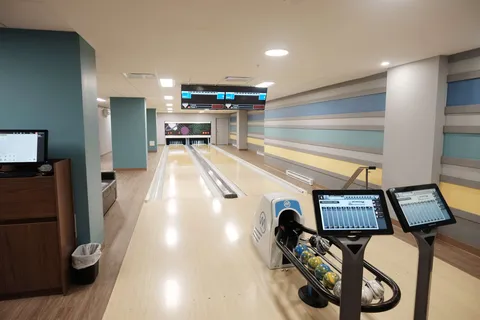 Indoor bowling lanes with a ball return and screens.