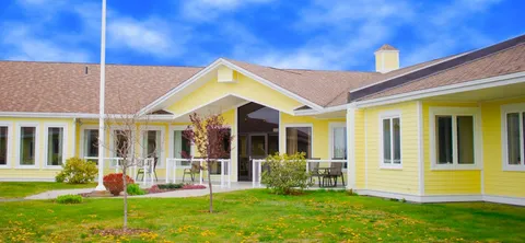 Yellow building with a covered entrance, white railings and a lawn