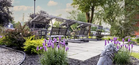 Garden patio with covered seating, flowers and mature trees.