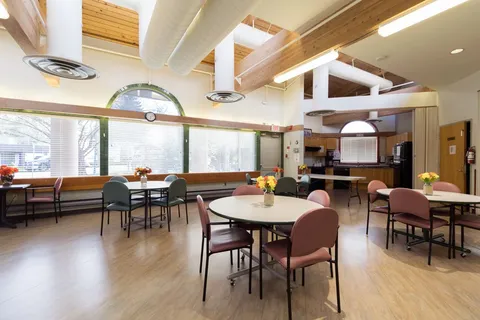 Round dining tables and chairs beneath timber beams and tall windows