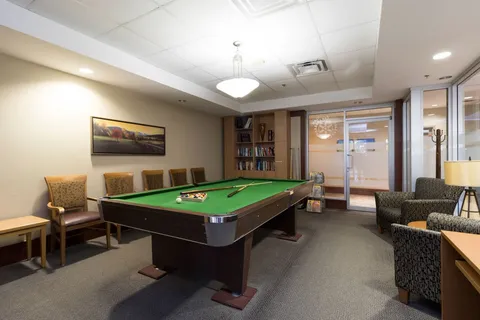 Pool table with cues and balls beside upholstered chairs and bookshelves