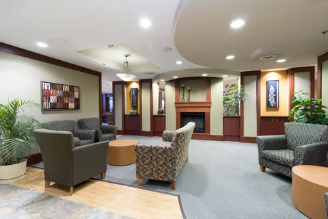 Room with armchairs, wooden tables, a fireplace and tree-patterned wall art