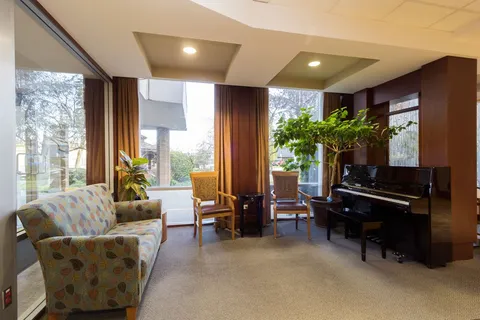 Upright piano, patterned sofa and chairs beside tall windows