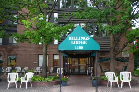 Brick residence entrance with a green canopy, white chairs and trees