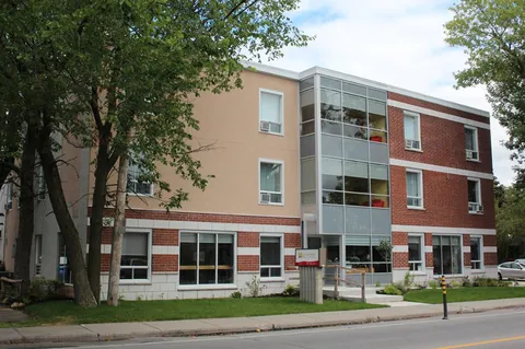 Brick residence with a glass stairwell, front walkway and mature trees.