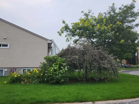 Side of a white building beside a lawn, shrubs and a covered doorway