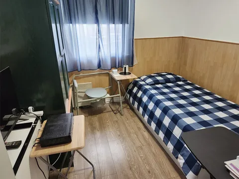 Bedroom with a blue and white checked bedspread, bedside tables, a television and a chair