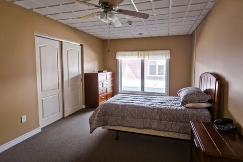 Bedroom with a bed, dresser, white closet doors and a ceiling fan