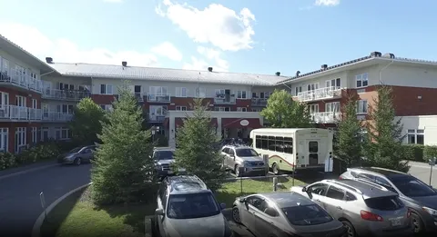 Multistorey building with balconies, trees and a parking area with cars and a minibus