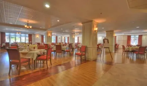 Dining tables and red upholstered chairs beside columns and wide windows
