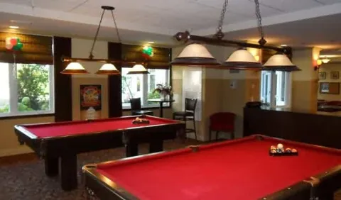 Two red billiard tables beneath pendant lights beside windows and chairs