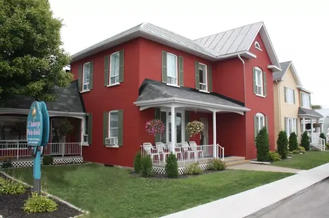 Red two-storey residence with white porch railings and a front lawn