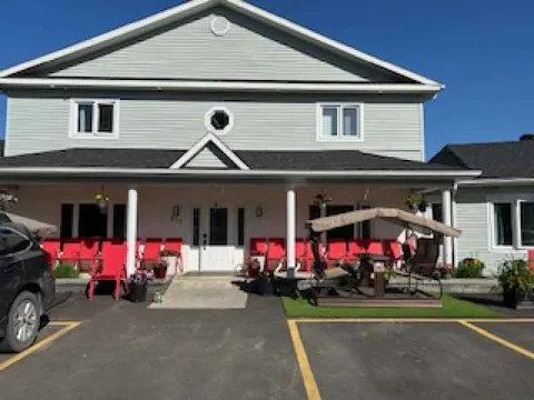 Residence facade with covered porch, red chairs, planters and a bench swing