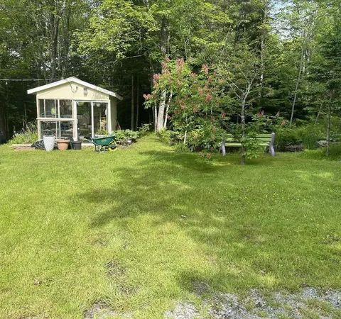 Garden lawn with a small greenhouse, benches and trees