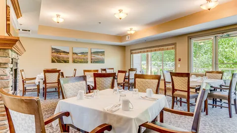 Dining room with set tables beside tall windows and a fireplace.