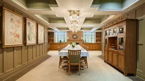 Dining room with a long table, upholstered chairs, wood cabinets and floral artwork.