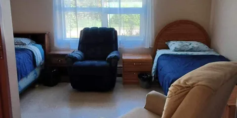 Bedroom with two beds, two armchairs, a bedside cabinet and a large window