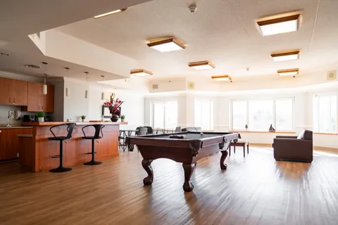 Room with a pool table, bar counter, stools and an armchair