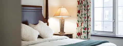 Bed and bedside lamp beside a window with patterned curtains